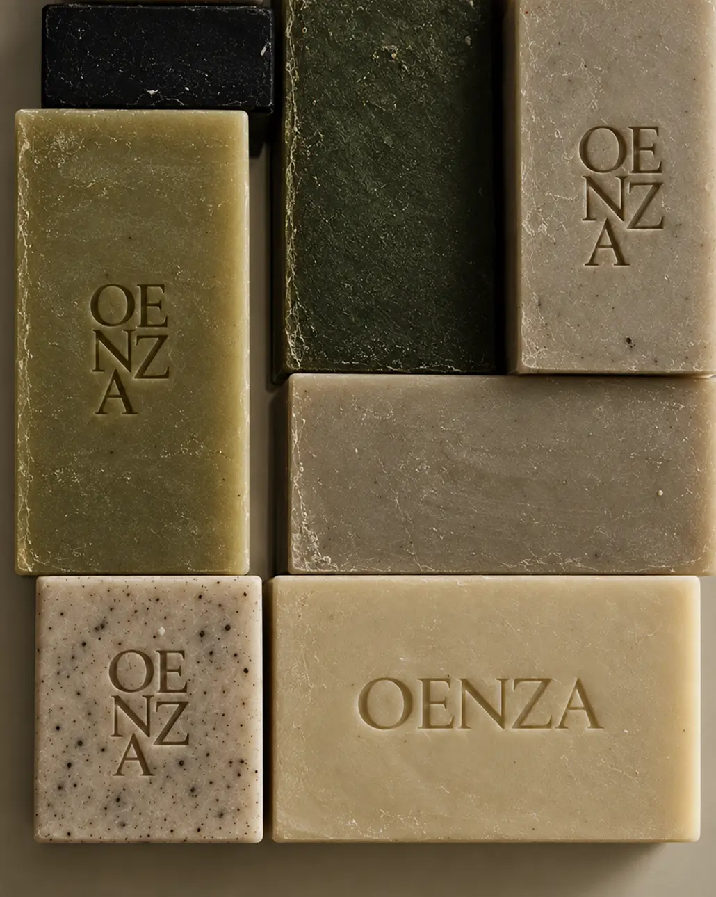 RHEA Creative Several rectangular bars of soap in various neutral colors are arranged together, with most bars embossed with the word “OENZA.”. Luxury Branding